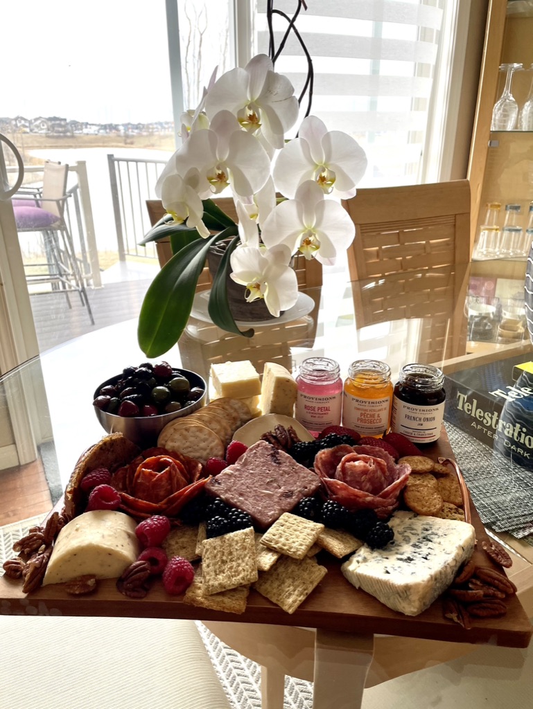 A charcuterie board arranged with cheeses, cured meats, berries, crackers, olives, nuts and preserves.