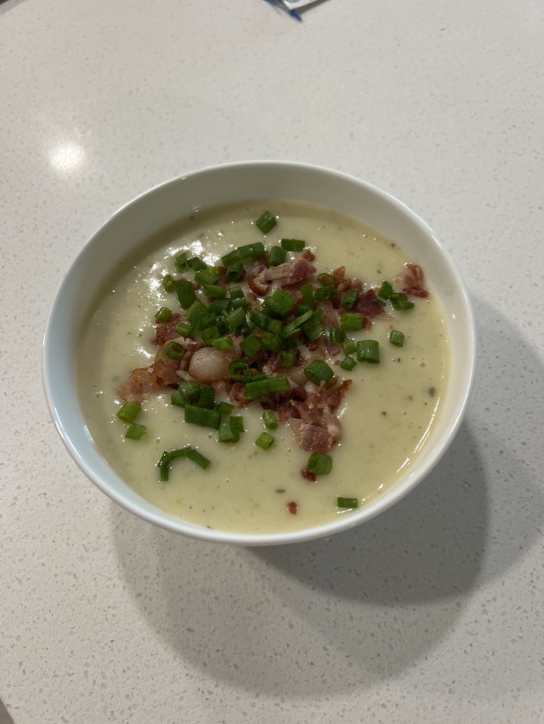 A finished bowl of creamy soup topped with bacon and green onions.