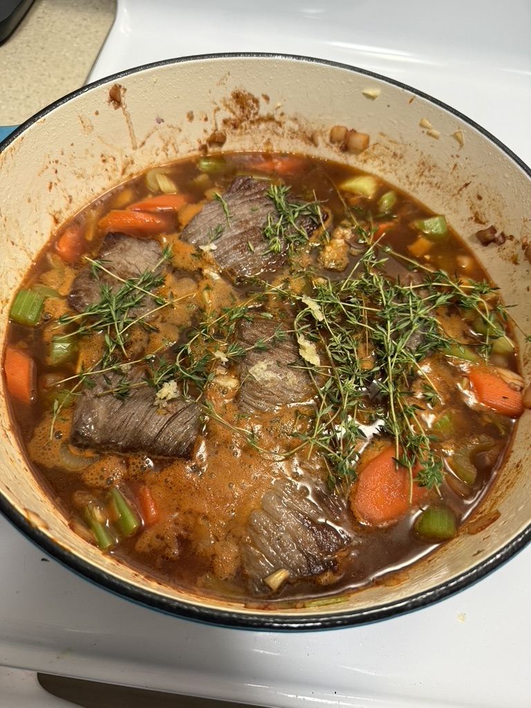 Beef, carrots, celery and herbs cooking together in a large pot.